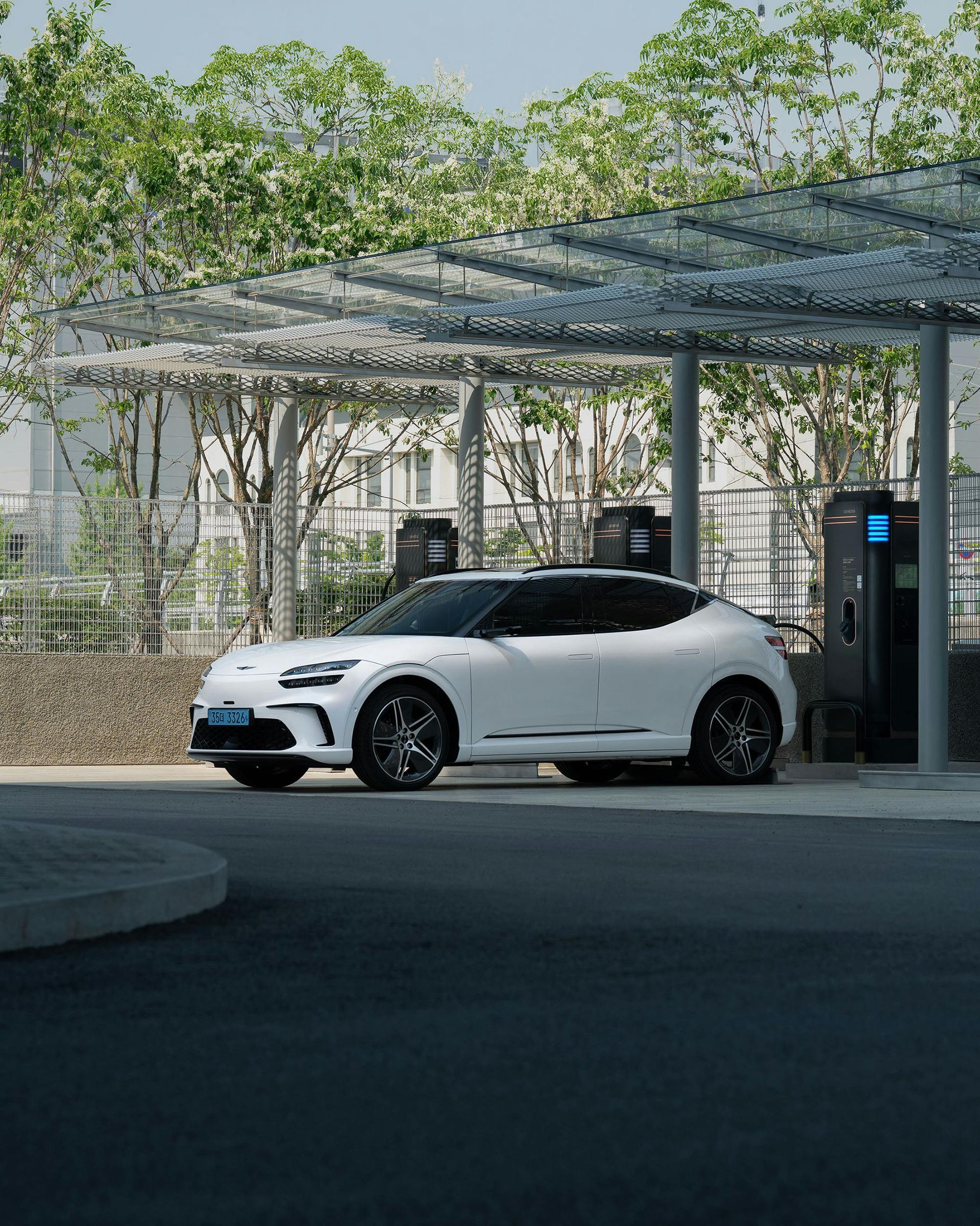 White electric vehicle parked at a charging station under a metal canopy.