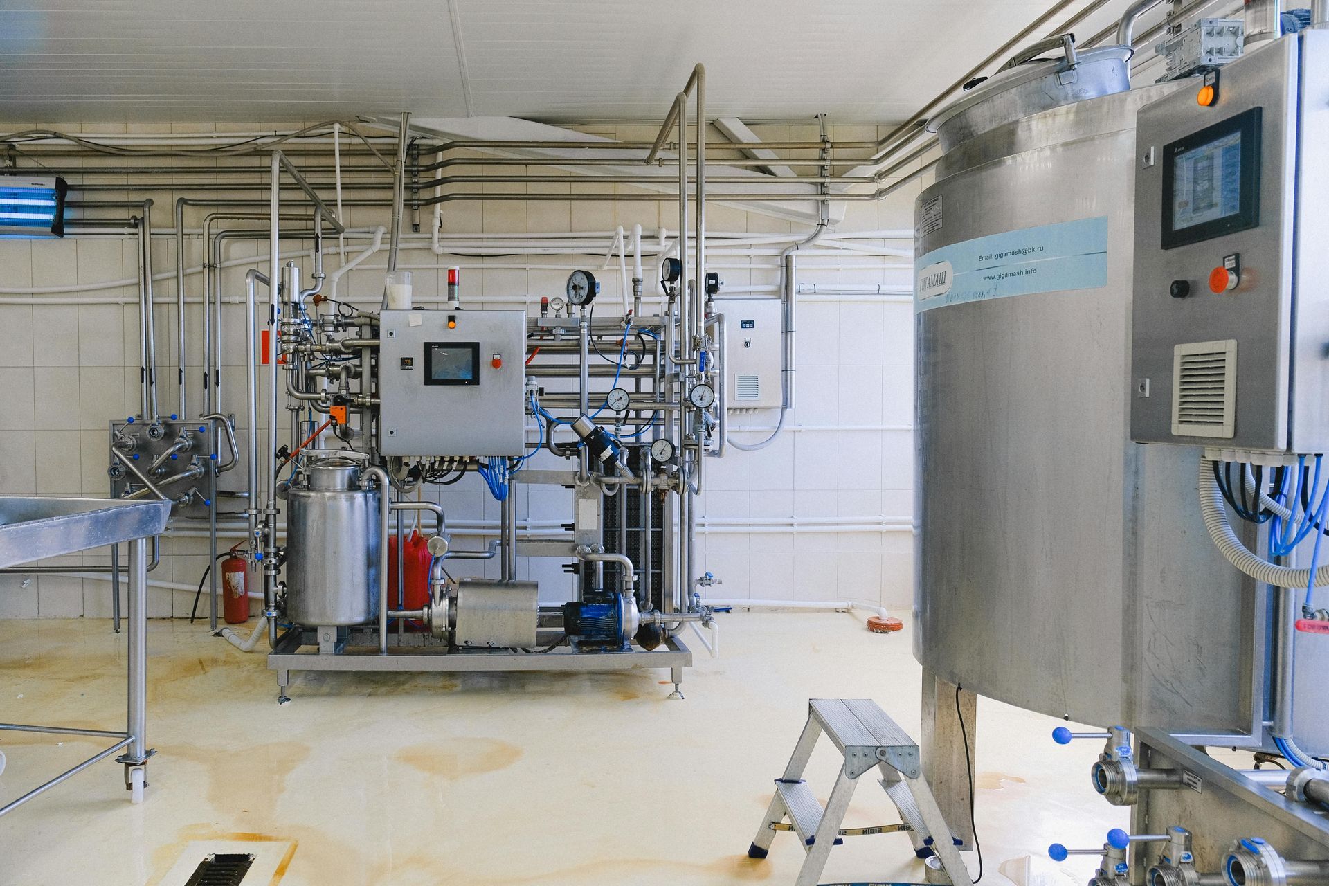 Industrial processing equipment in a clean white room with steel tanks, pipes, and control panels.