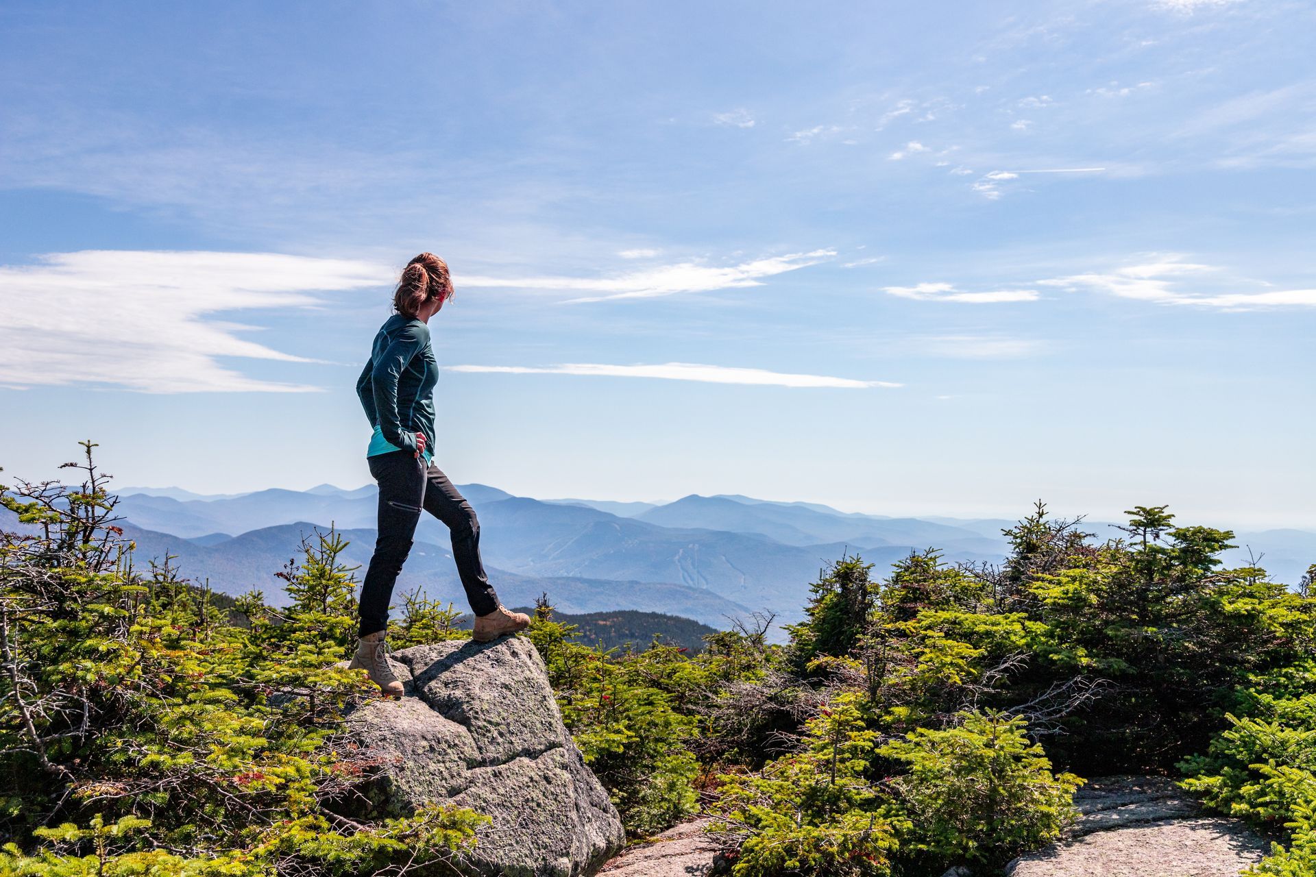 A woman is standing on a rock on top of a mountain.
