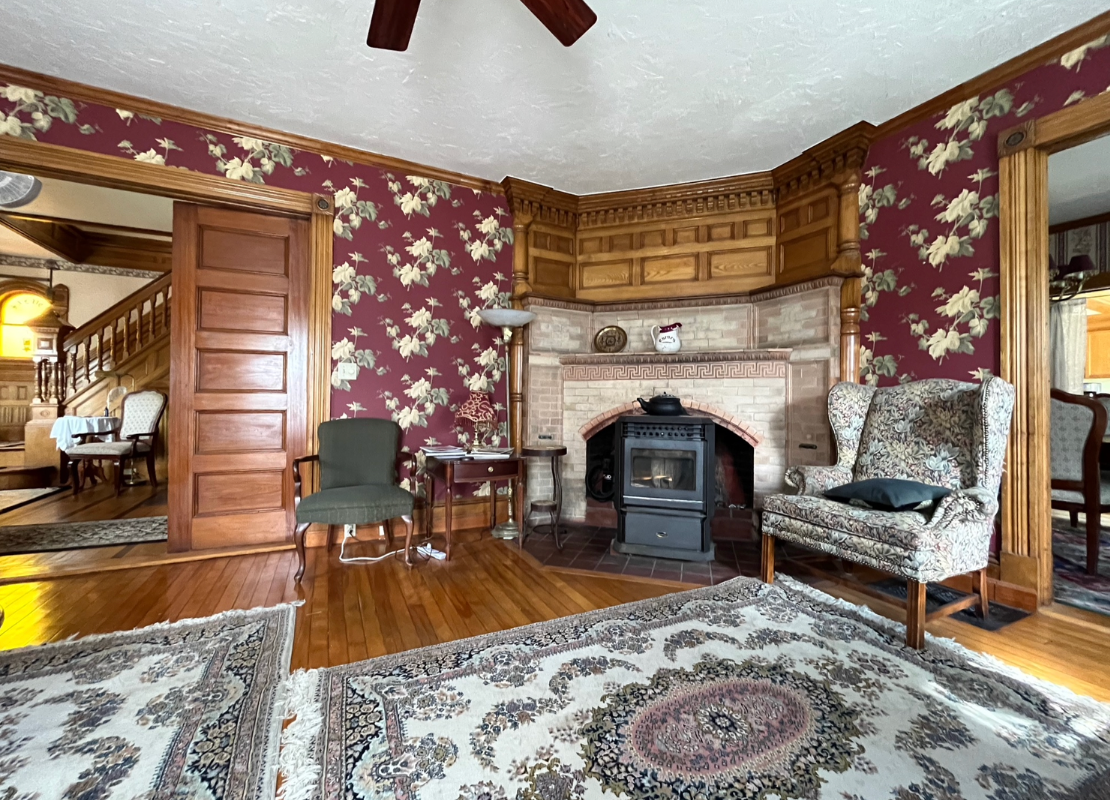 A living room with a fireplace , chairs , a rug and a ceiling fan.