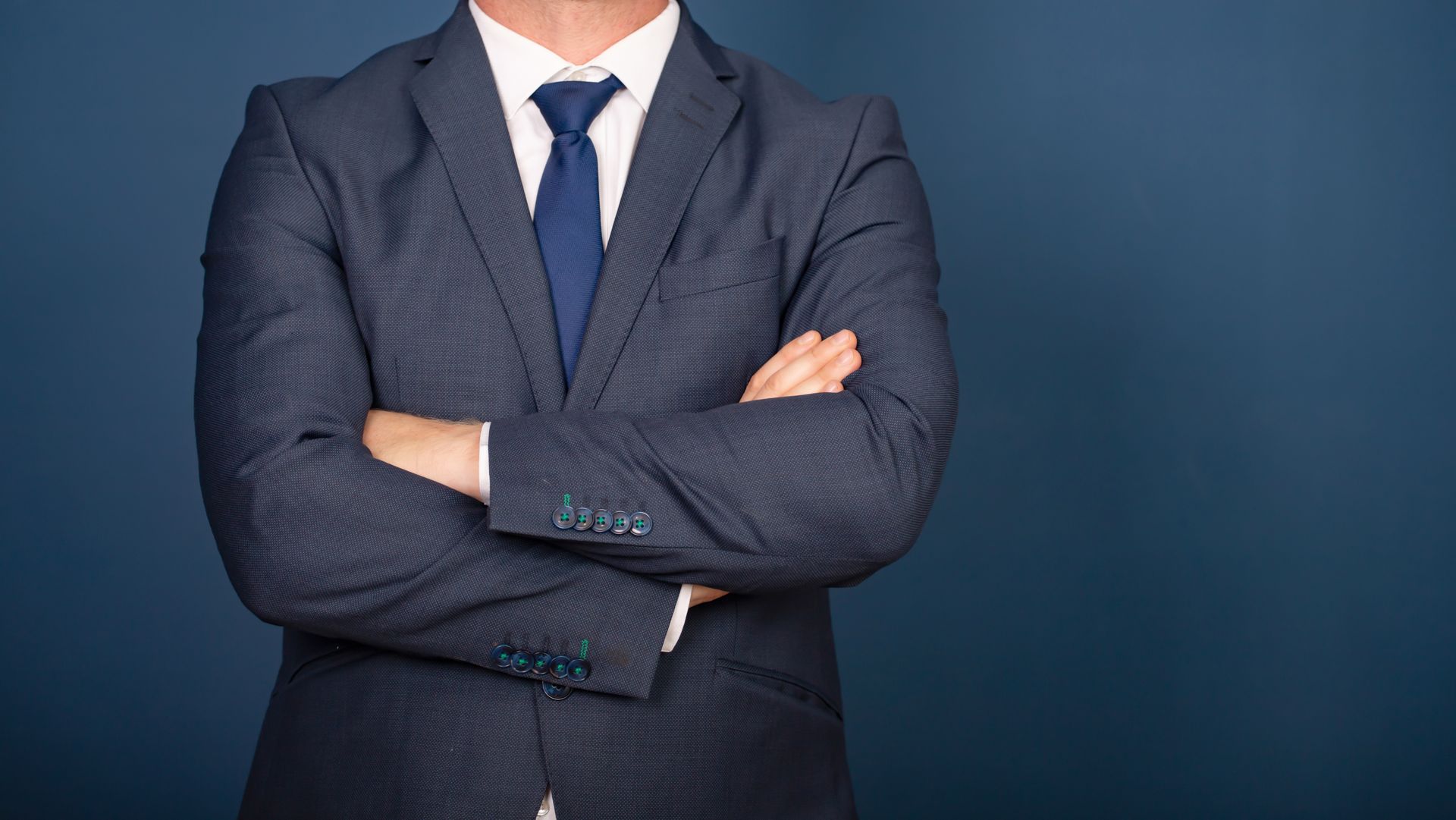 Businessperson in a dark suit with arms crossed against a blue background