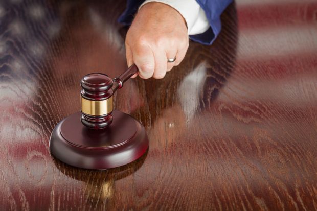 Judge’s hand holding a gavel over a wooden courtroom desk