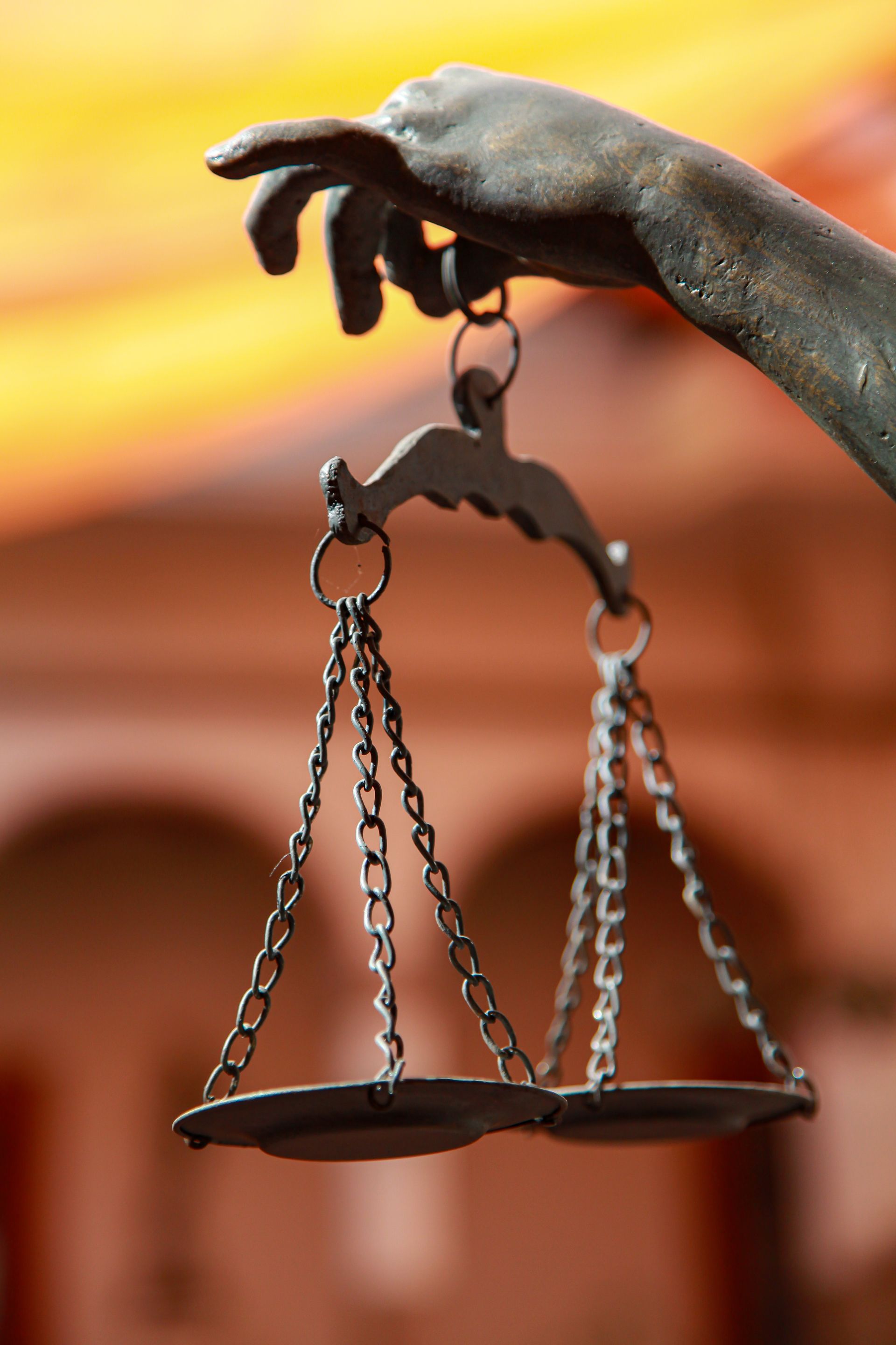Bronze justice scales held by a statue hand against a blurred courthouse background