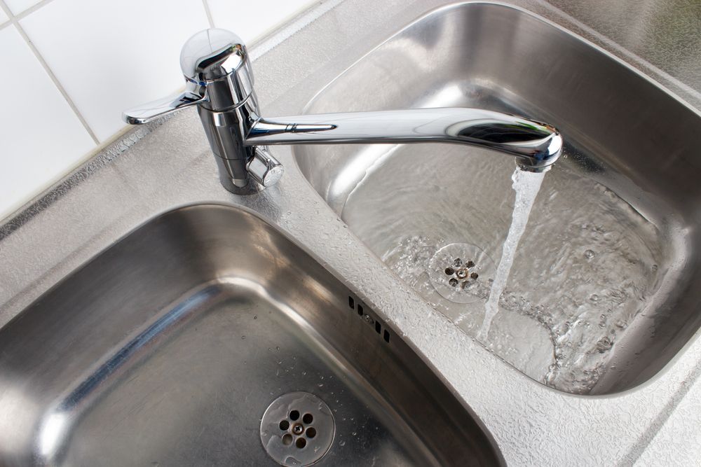 Water Flows From A Chrome Faucet Into A Stainless Steel Kitchen Sink Basin — DSR Plumbing Pty Ltd in Ashtonfield, NSW