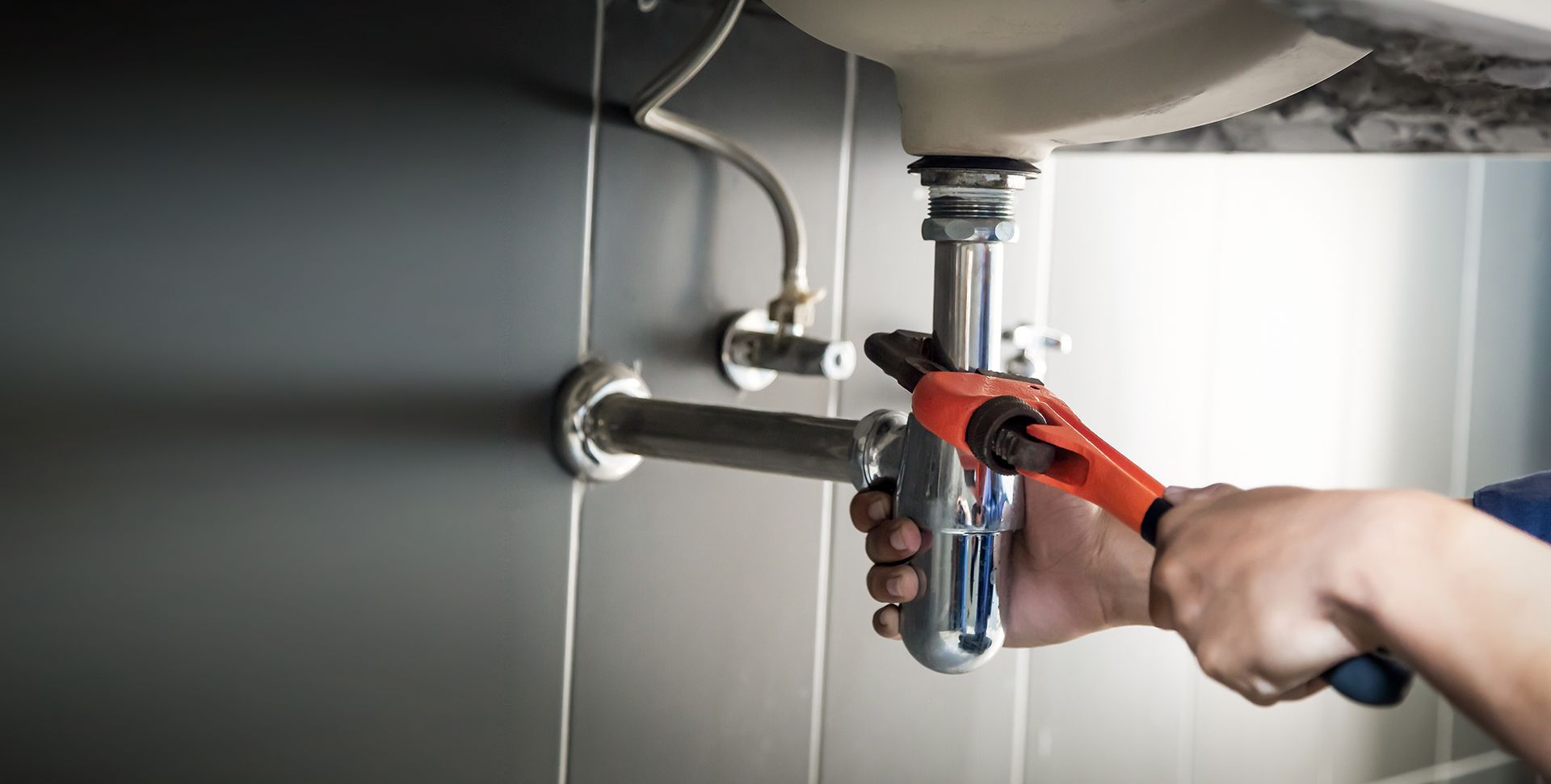 Plumber Using A Wrench To Repair A Chrome Drain Pipe — DSR Plumbing Pty Ltd in Thornton, NSW