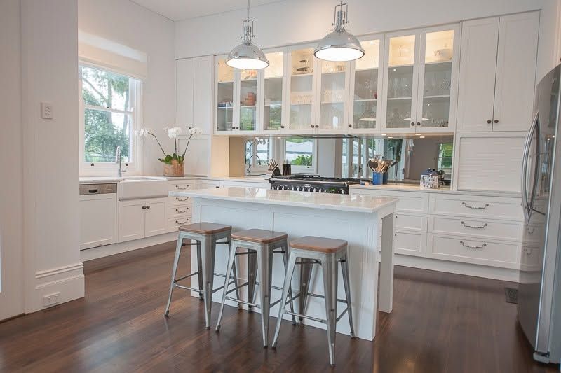 Bright White Kitchen With Island, Bar Stools, Pendant Lights, and Dark Wood Floors — DSR Plumbing Pty Ltd in Ashtonfield, NSW