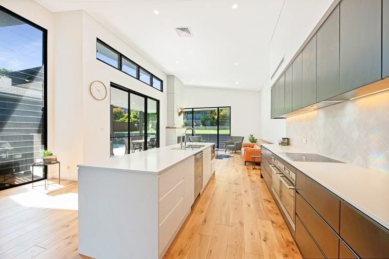 Bright Modern Kitchen With White Island, Wood Floors, and Large Windows — DSR Plumbing Pty Ltd in Ashtonfield, NSW