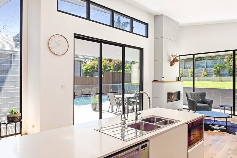 Bright Modern Kitchen and Living Room With Large Sliding Glass Doors and Fireplace — DSR Plumbing Pty Ltd in Ashtonfield, NSW