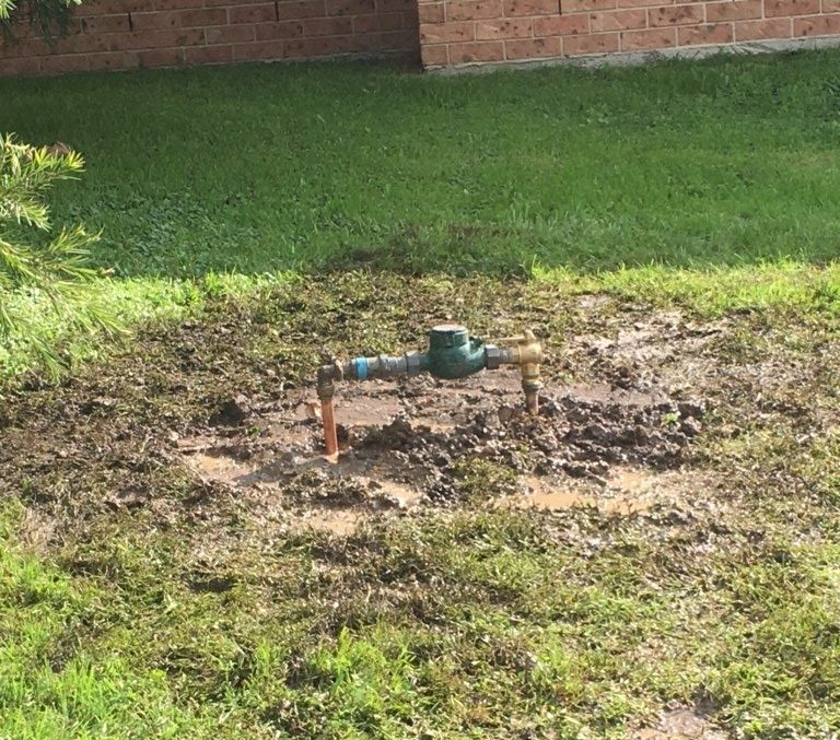 Water Meter Assembly Mounted on Pipes Above a Muddy Patch of Ground — DSR Plumbing Pty Ltd in Ashtonfield, NSW