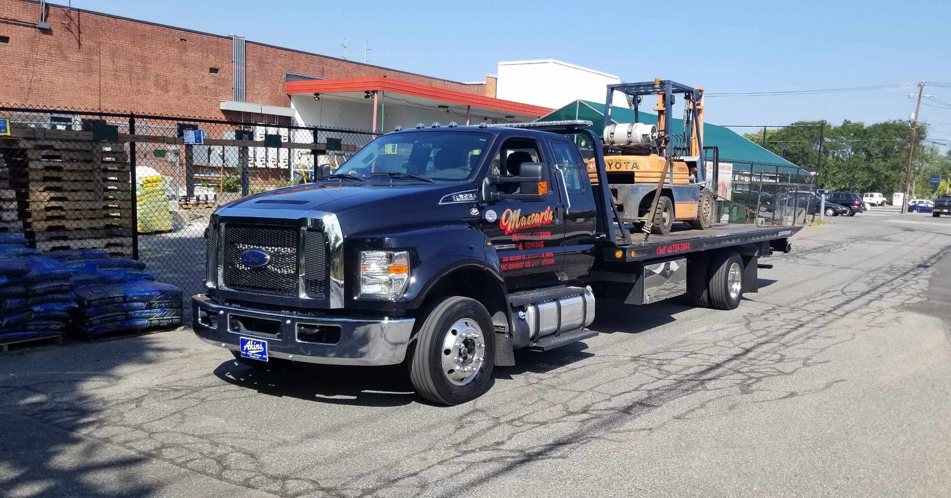 A tow truck with a forklift on the back is parked on the side of the road.