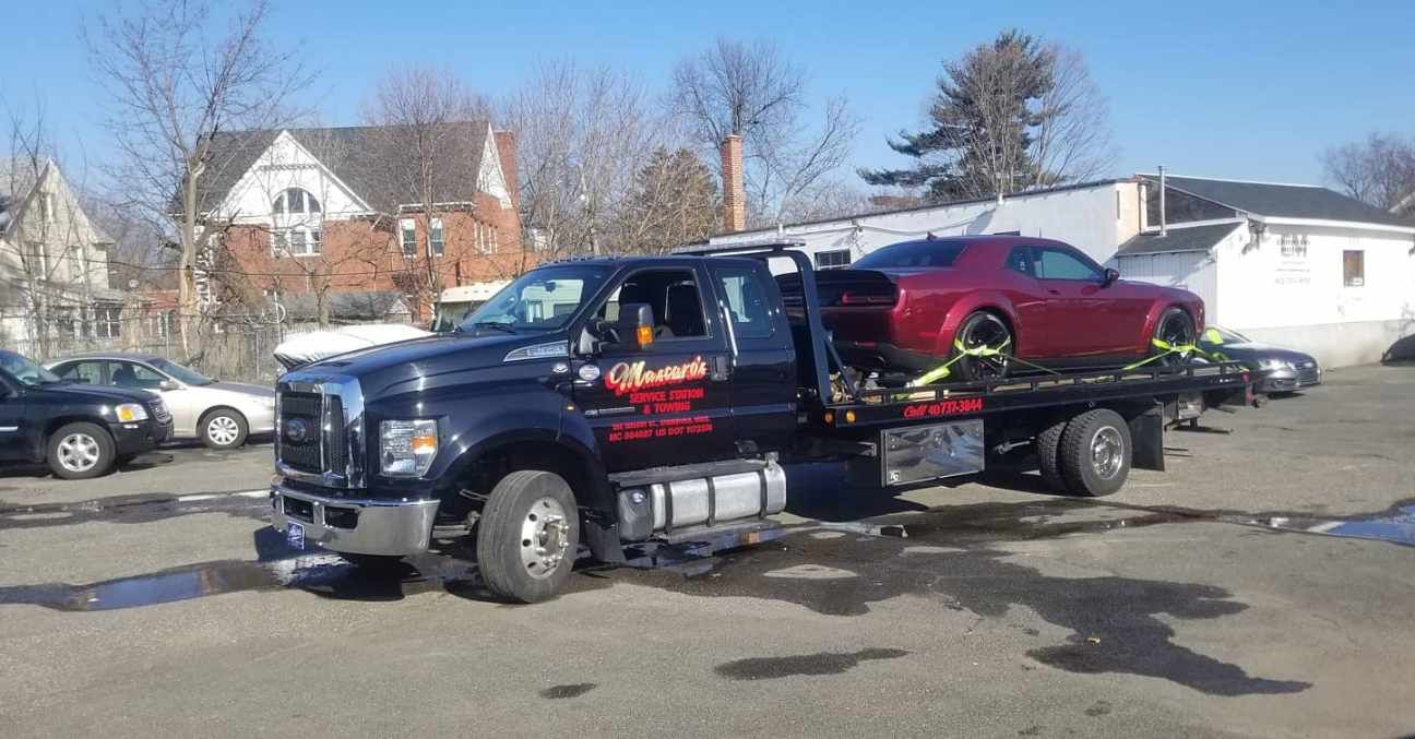 A tow truck is towing a red car in a parking lot.