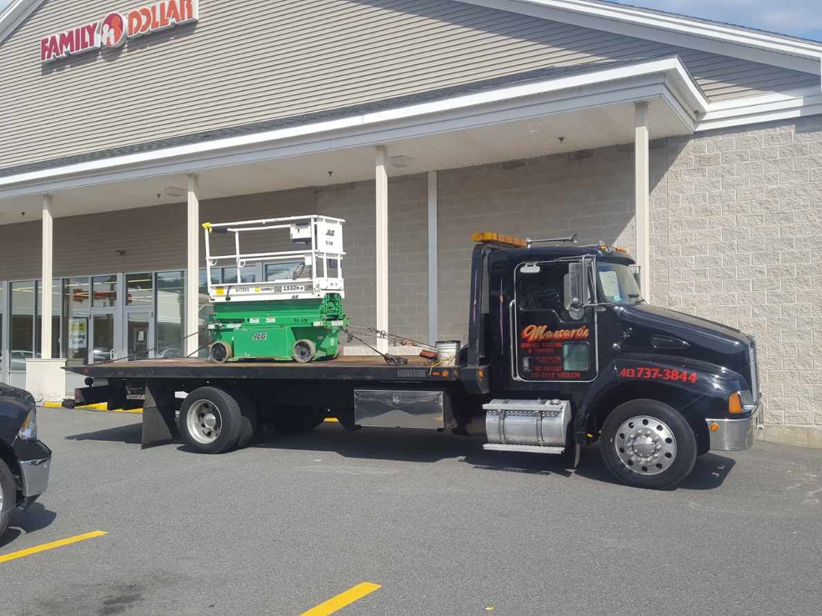 A flatbed tow truck is parked in front of a store.