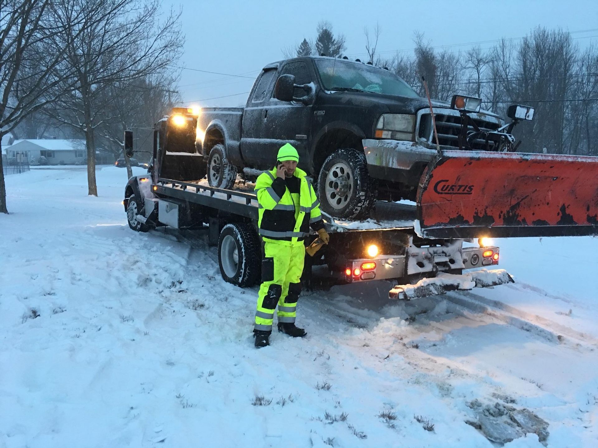 A man is standing in front of a tow truck in the snow.