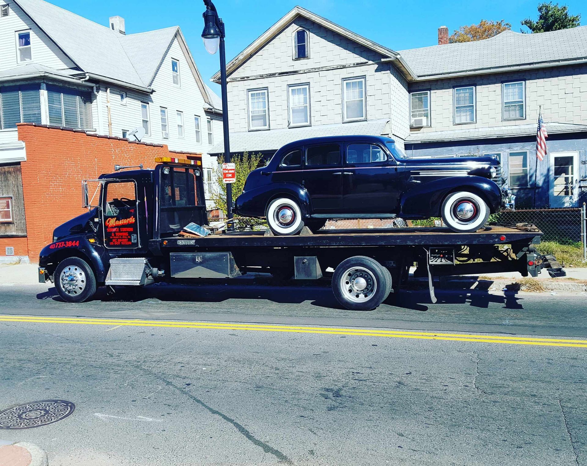 A tow truck is carrying a black car on the back of it.