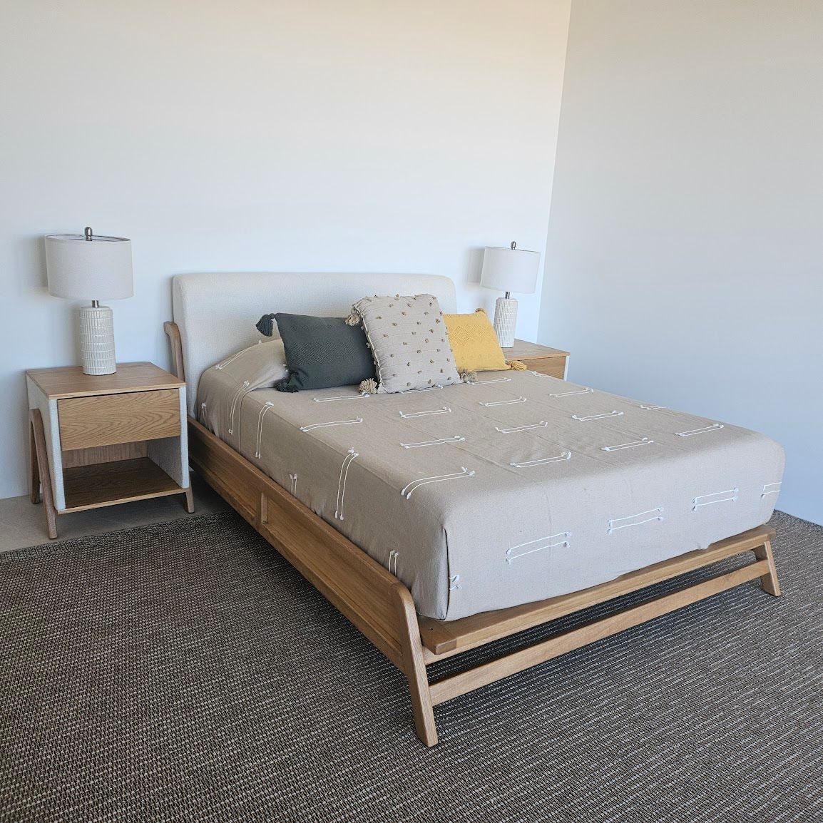 Dormitorio minimalista con cama de madera, mesitas de noche, lámparas blancas y alfombra tejida.