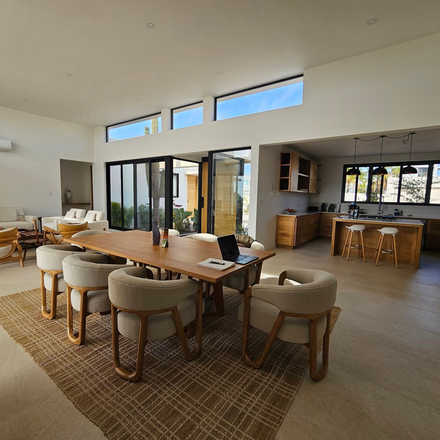 Comedor moderno de planta abierta con mesa larga de madera, sillas acolchadas y grandes puertas de cristal.