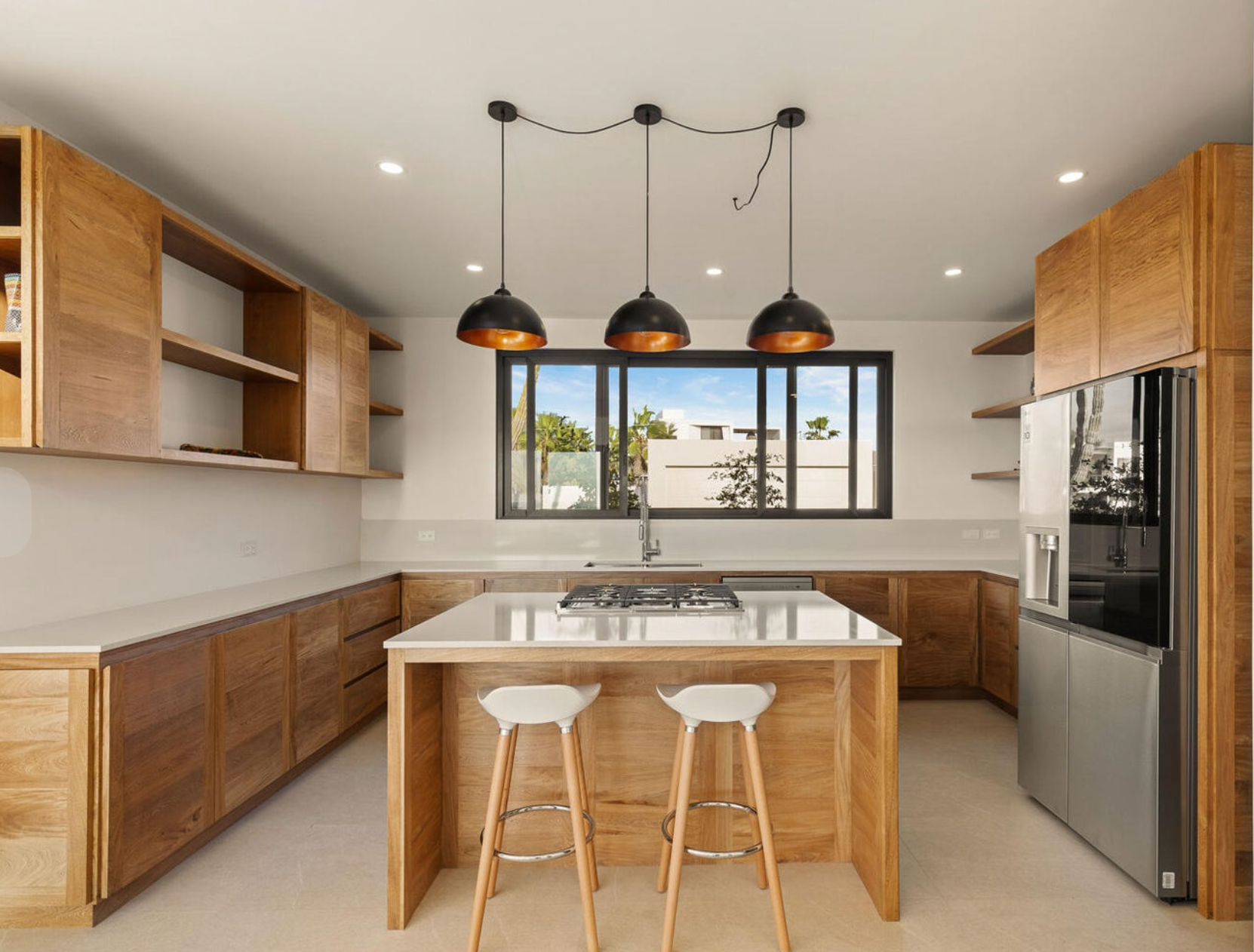 Cocina moderna con gabinetes de madera, isla con asientos, electrodomésticos de acero inoxidable y lámparas colgantes.