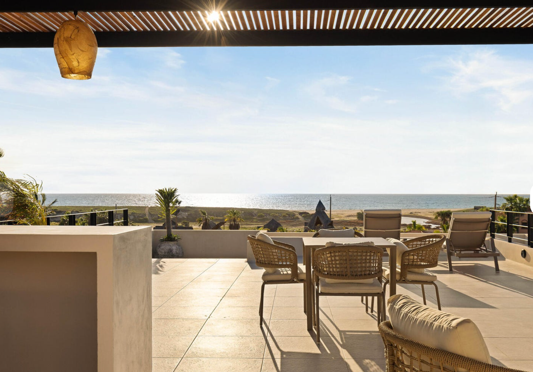 Terraza en la azotea con asientos de mimbre, vista al mar y brillante luz del sol de la tarde.