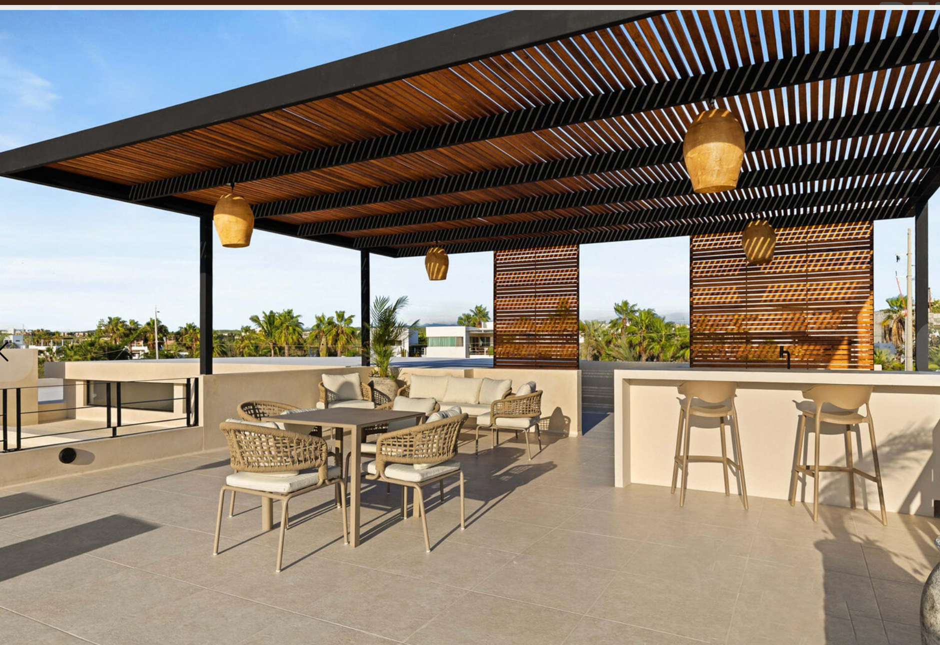 Moderna terraza en la azotea con sillones, taburetes de bar y un toldo de madera con listones con vistas al agua.