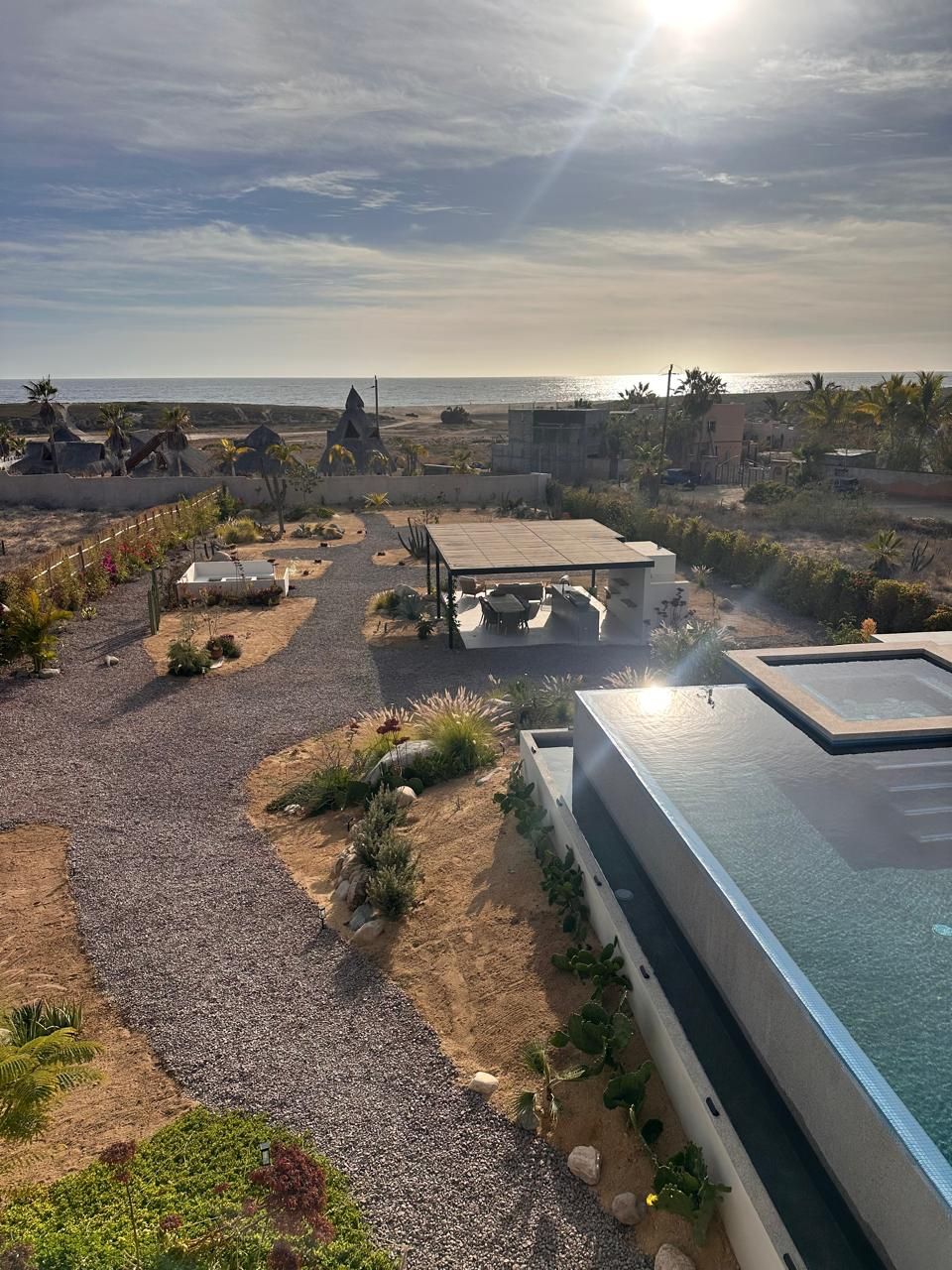 Piscina en la azotea bañada por el sol, con vistas al jardín de grava y al océano al atardecer.