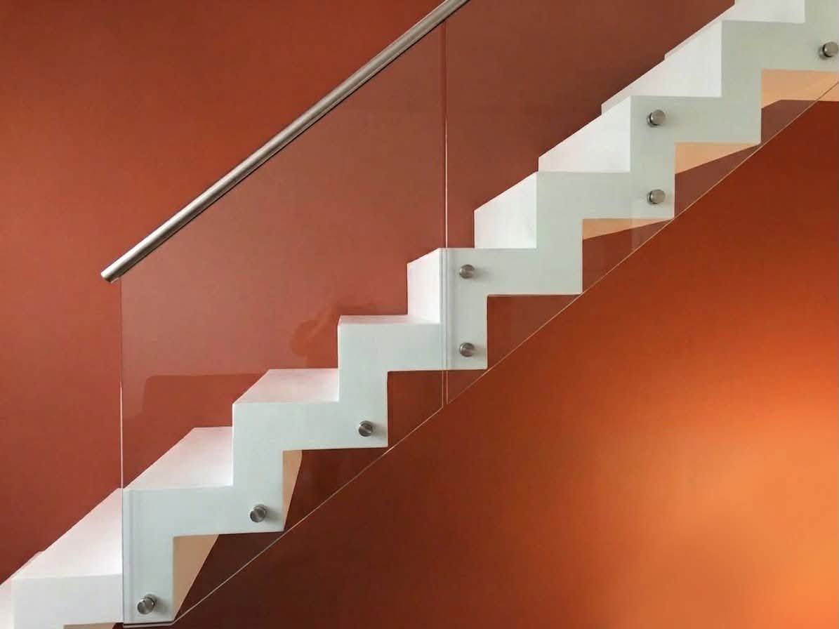 Scala bianca a zigzag con corrimano in metallo, addossata a una parete arancione.