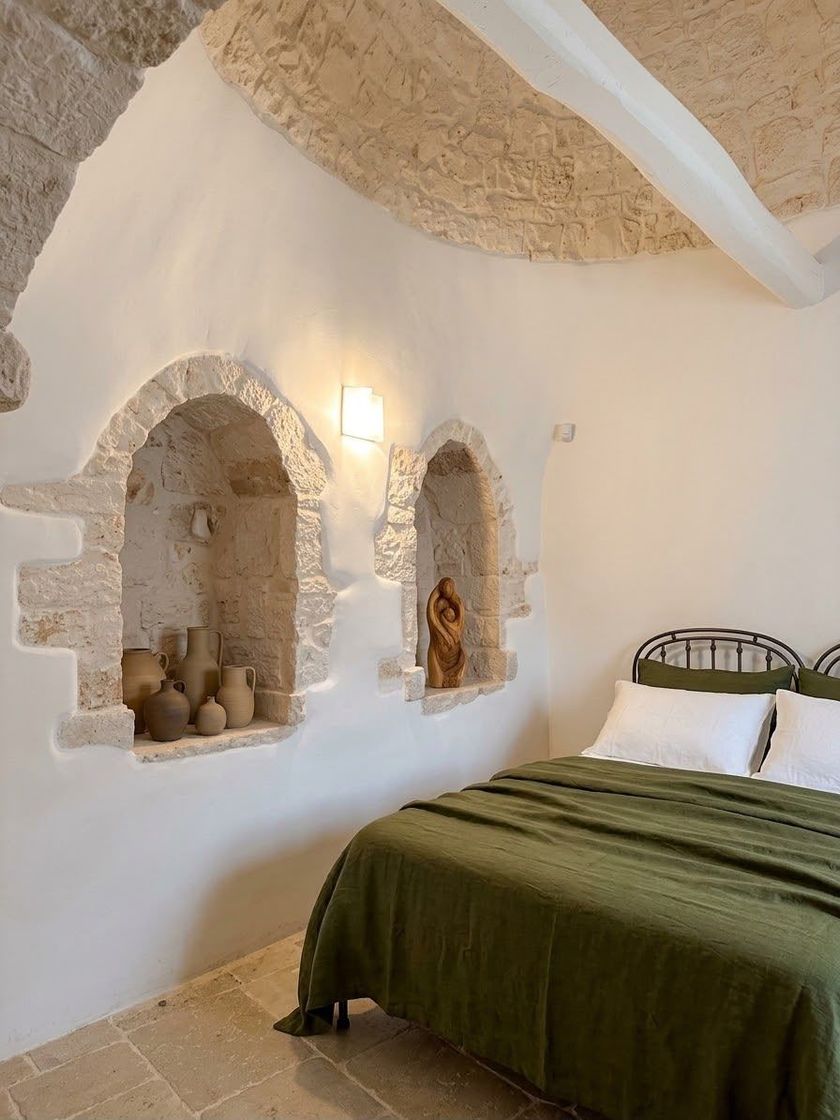 Accogliente camera da letto in stile grotta, con pareti bianche, nicchie ad arco e copriletto verde