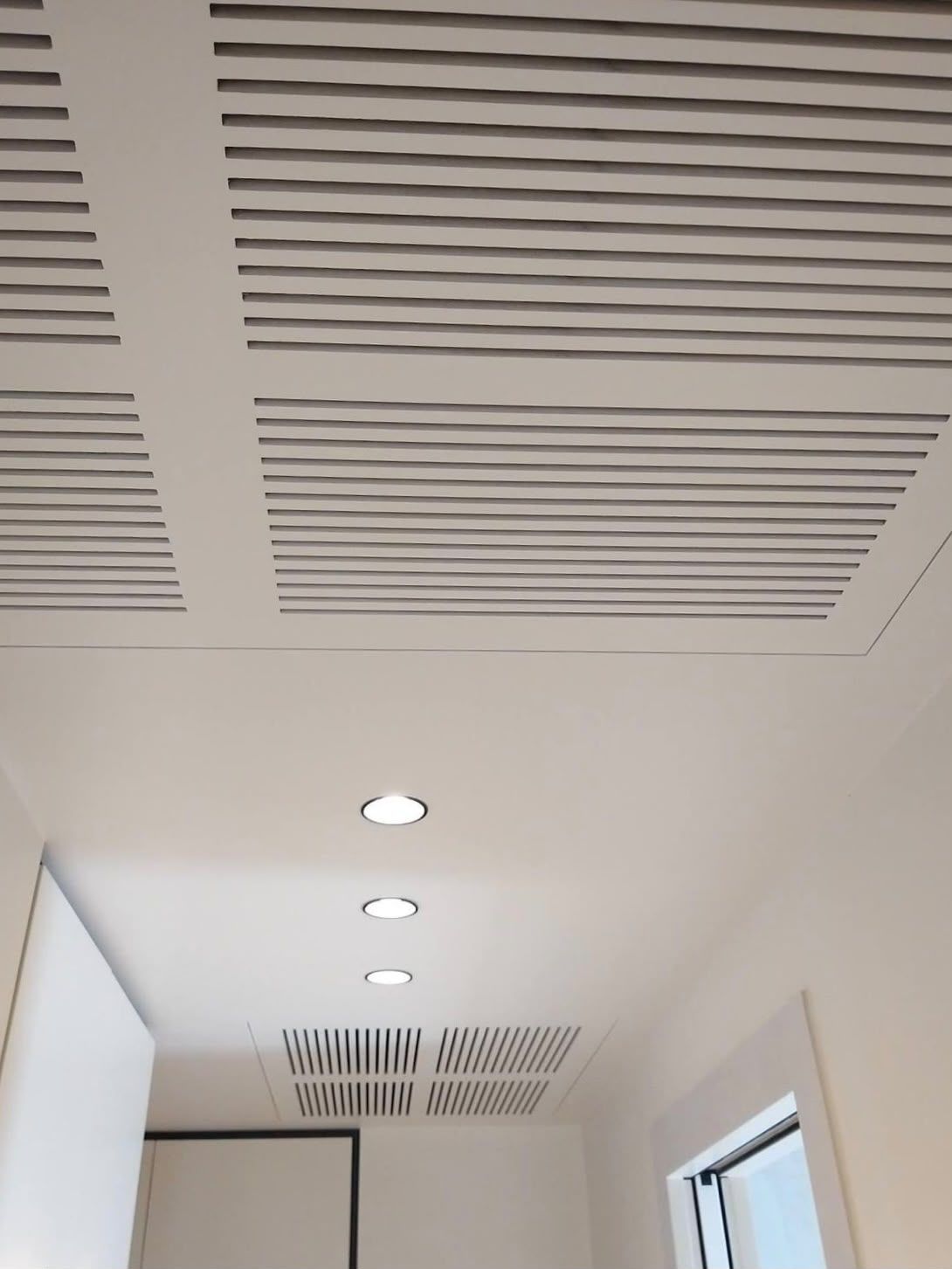 Soffitto con bocchette lineari, faretti a incasso e un lucernario sopra un corridoio