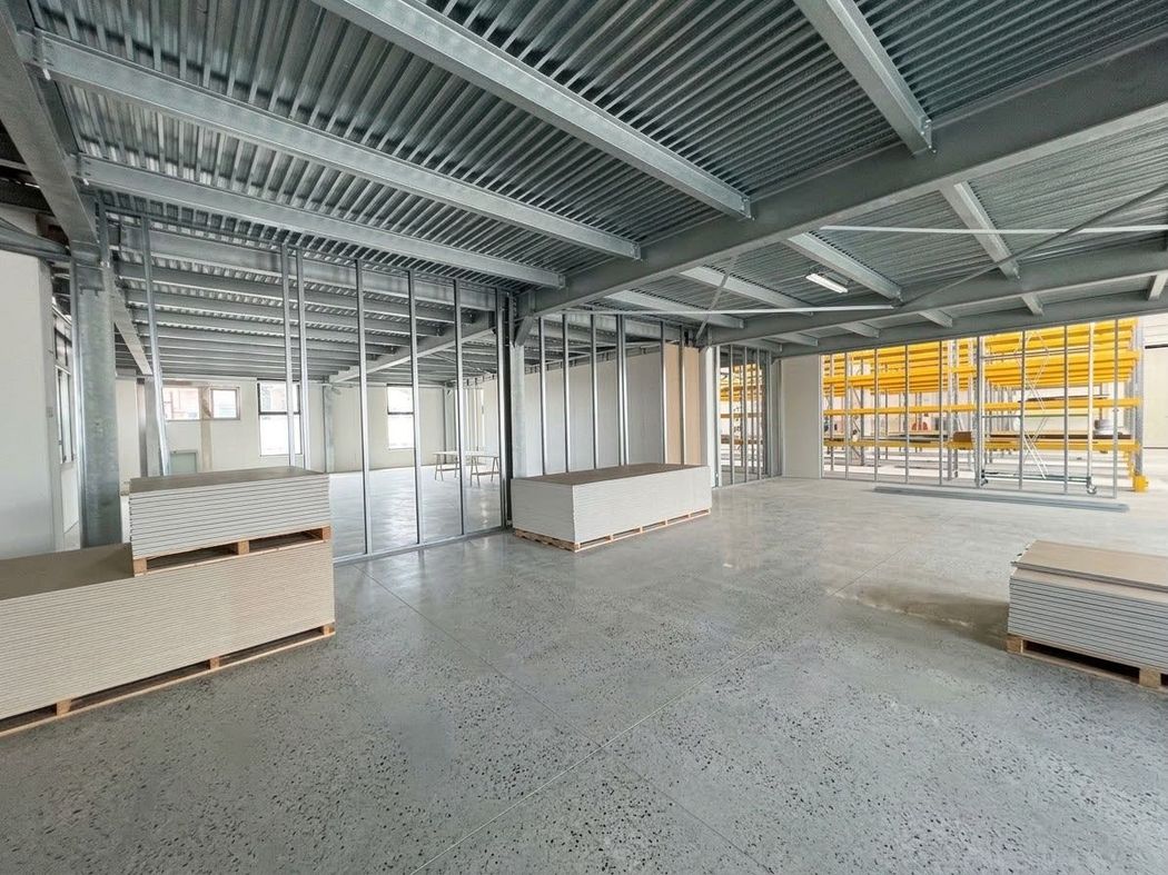 Interno industriale vuoto e incompiuto, con soffitto in metallo a vista, pavimento in cemento e materiali imballati accatastati nello spazio