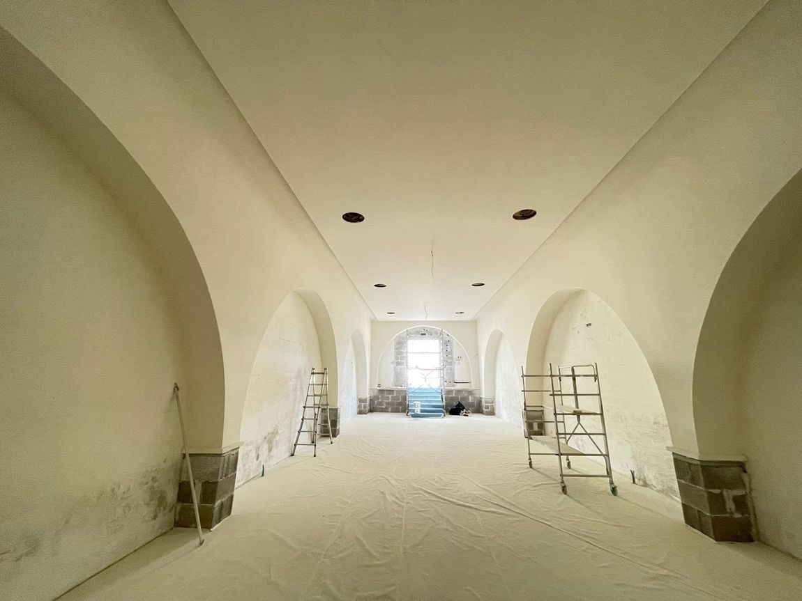 Corridoio ad arco in fase di ristrutturazione, con impalcature, pavimento coperto di polvere e luce proveniente da una finestra in lontananza