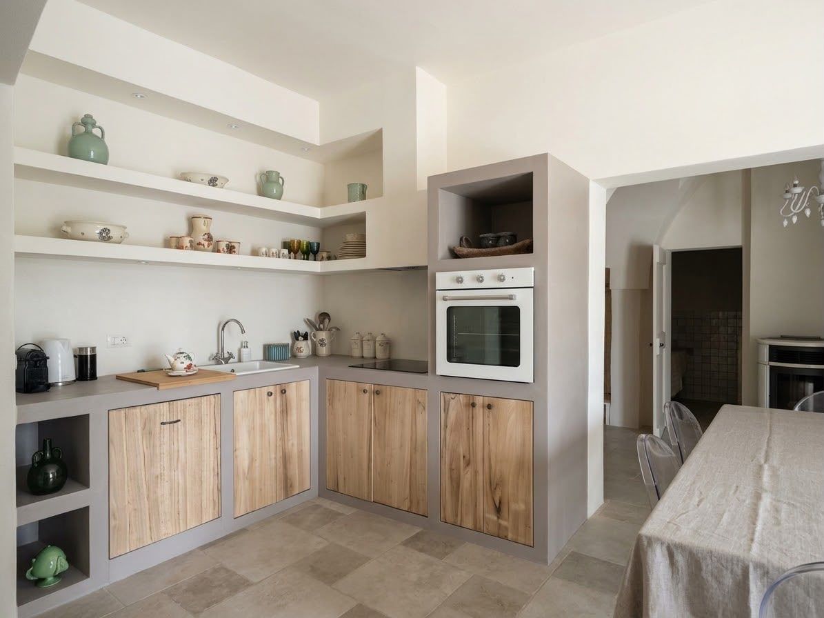 Cucina moderna e luminosa con mobili in legno, mensole bianche, forno da incasso e un tavolo da pranzo accanto