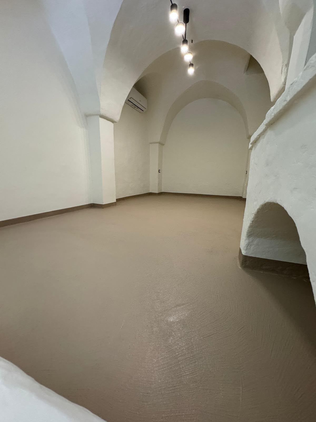 Stanza bianca e vuota con volta a botte e pavimento beige, illuminata da faretti a soffitto
