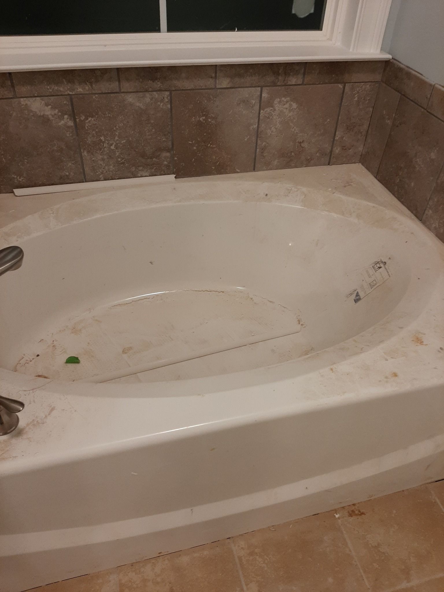 A dirty bathtub in a bathroom next to a window.