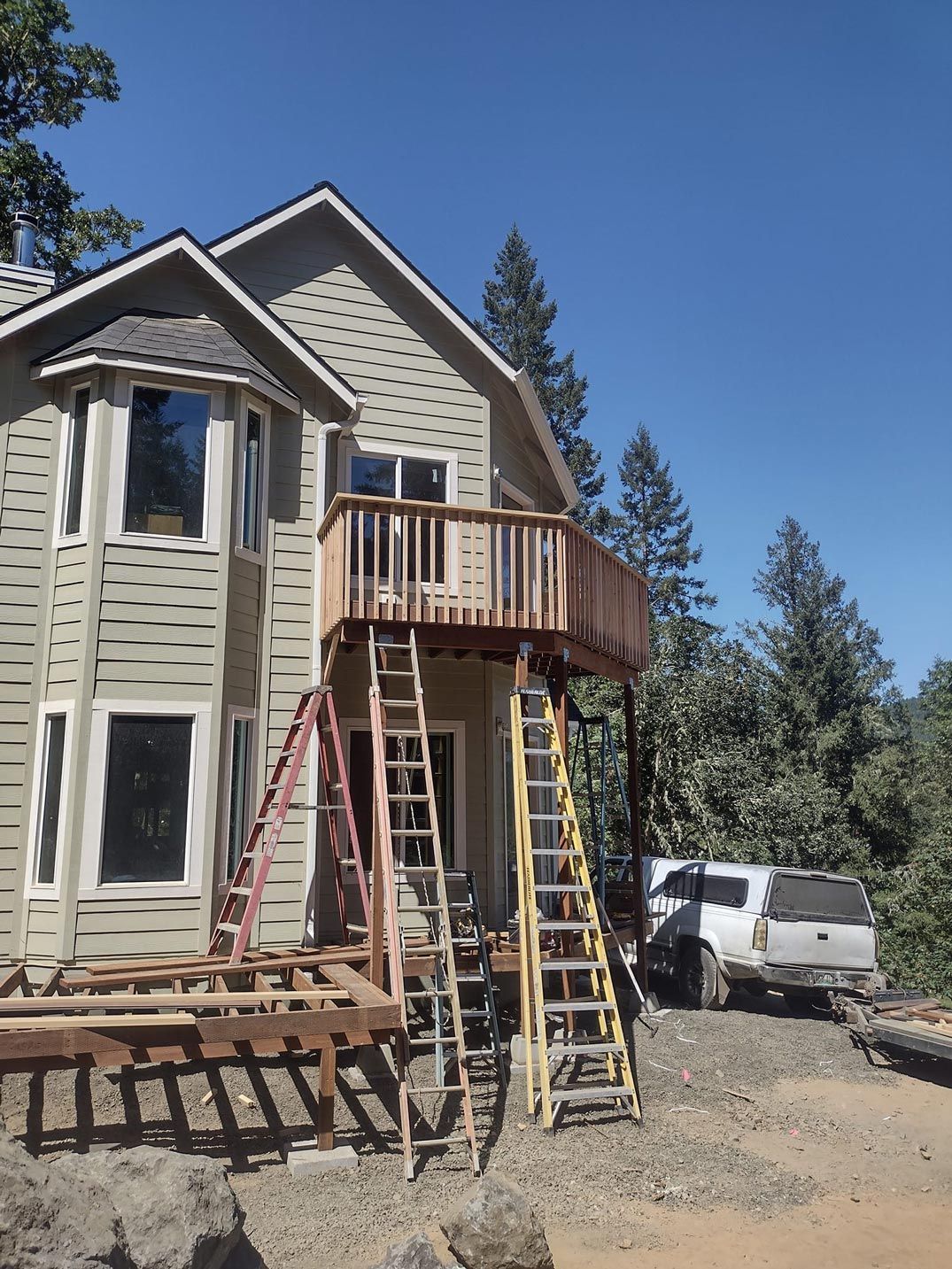Two-story house exterior with ladders and wooden deck under construction on a sunny day
