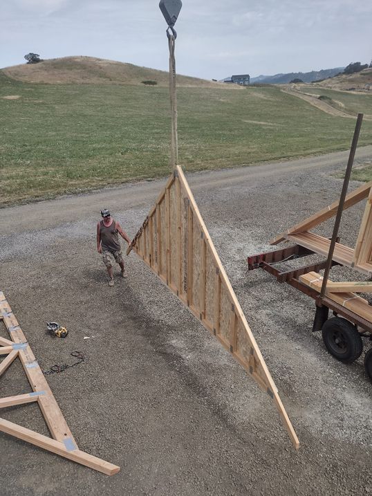 Construction site with a wooden triangular panel being hoisted by a crane over gravel.