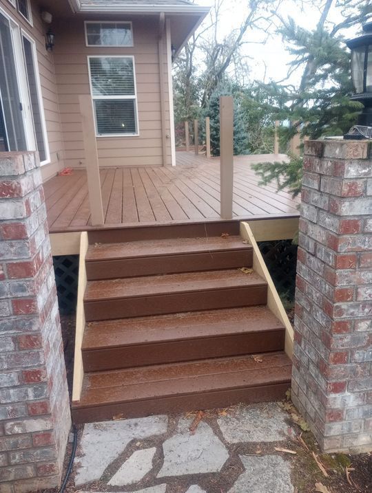 Front porch with wooden stairs between brick columns leading to a beige house.