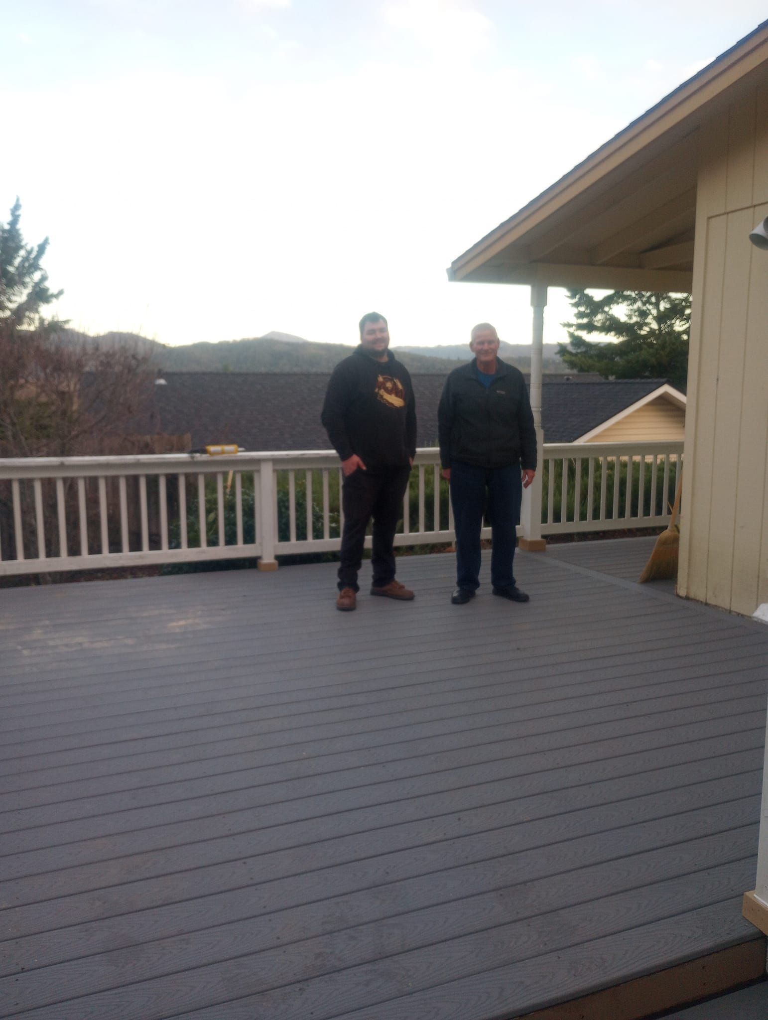 Two people standing on a wooden deck beside a house at sunset