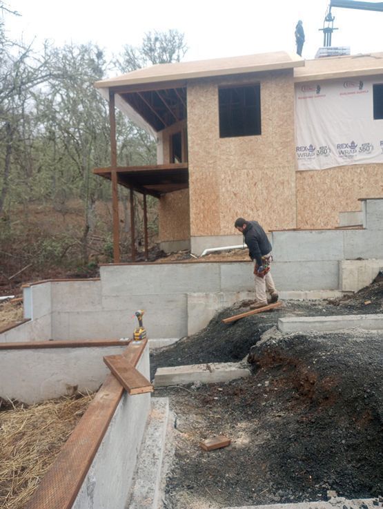 Construction site with two workers near a partially built house and a sloped concrete driveway