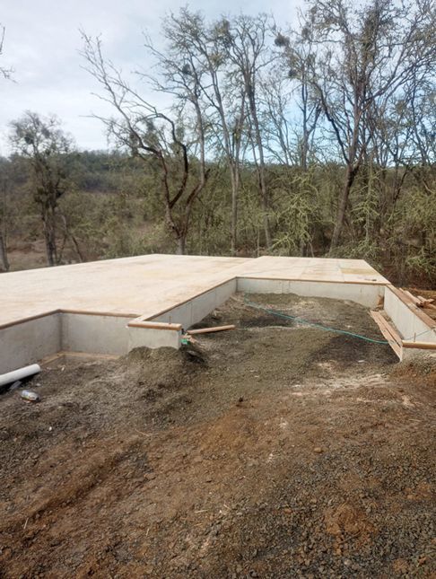 Concrete foundation slab under construction on a dirt lot with trees in the background.