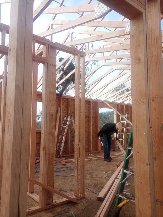 Wooden house frame under construction, with workers and scaffolding inside an unfinished structure.