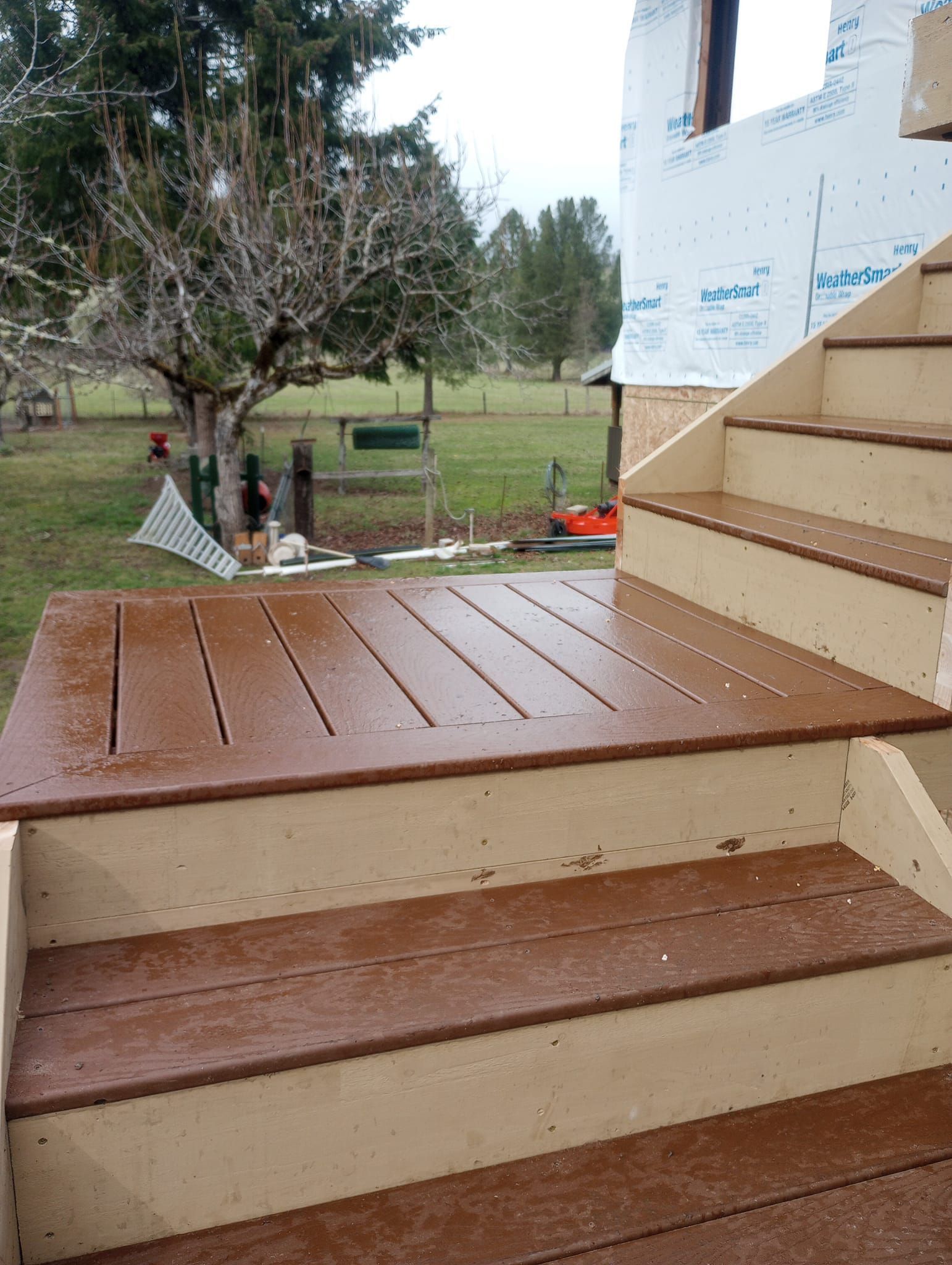 Outdoor wooden steps leading to a porch, with a yard and trees in the background