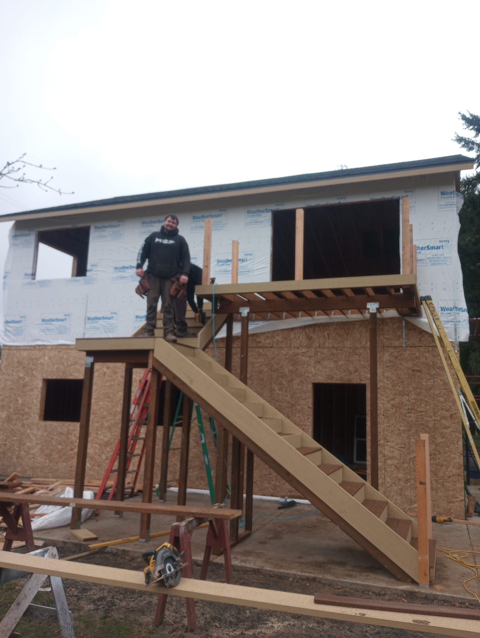 Worker on scaffolding building a two-story house with brick and white siding.