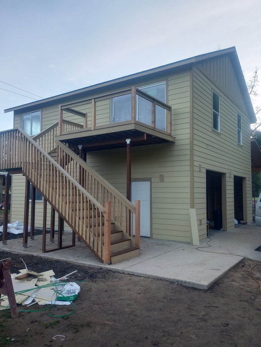 Two-story house exterior with green siding, a staircase, and a small balcony under construction