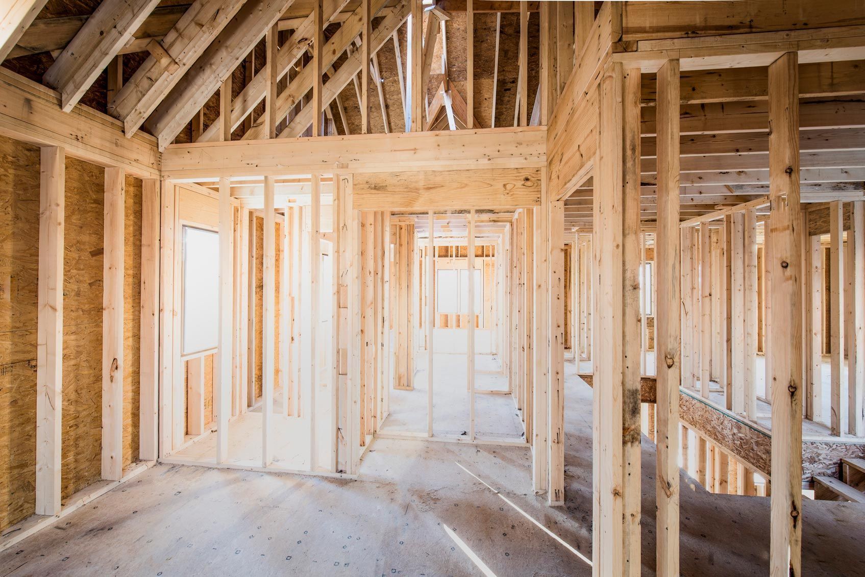 Wood-framed house interior under construction, with exposed studs and bright light through windows