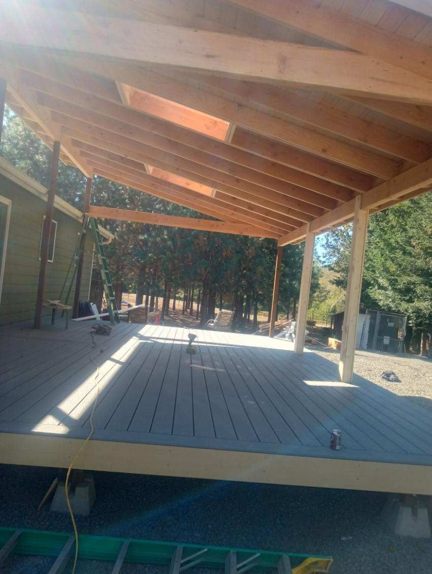 Outdoor wooden deck under a slanted roof, with trees visible beyond the open sides.