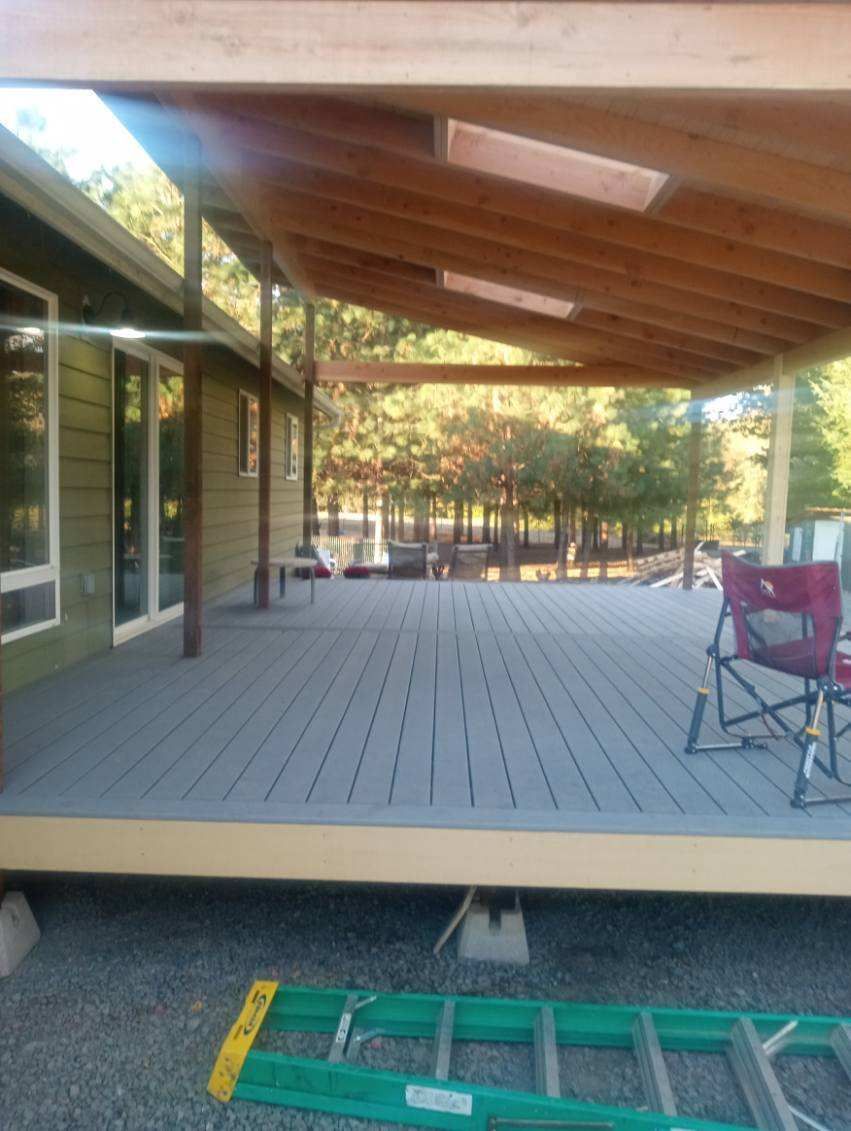 Covered wooden deck beside a house, with chairs and a ladder in the foreground.