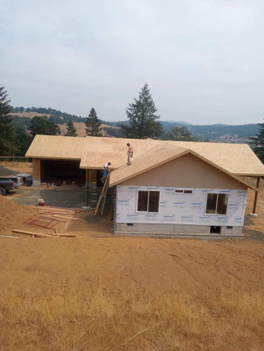 House under construction with unfinished roof and white siding in a dry rural landscape