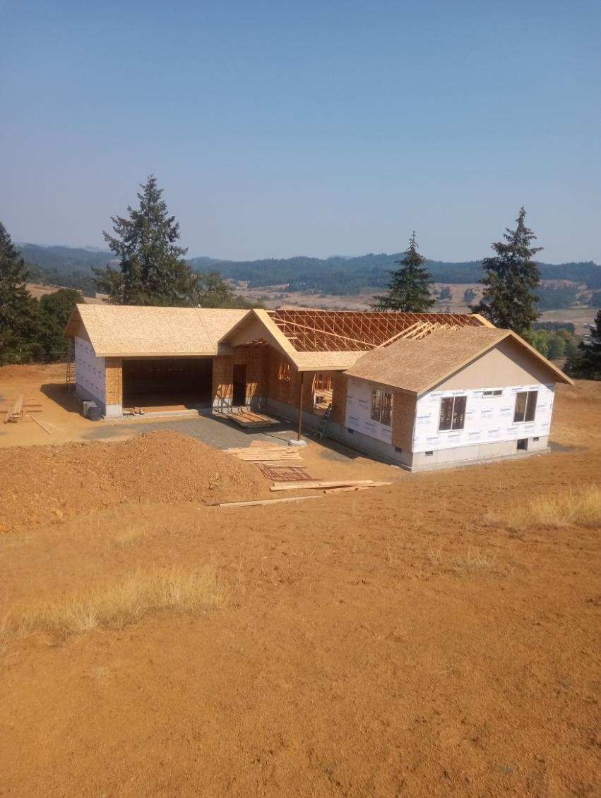 Partially built white house with a tan roof on a dirt lot, trees and hills in the background