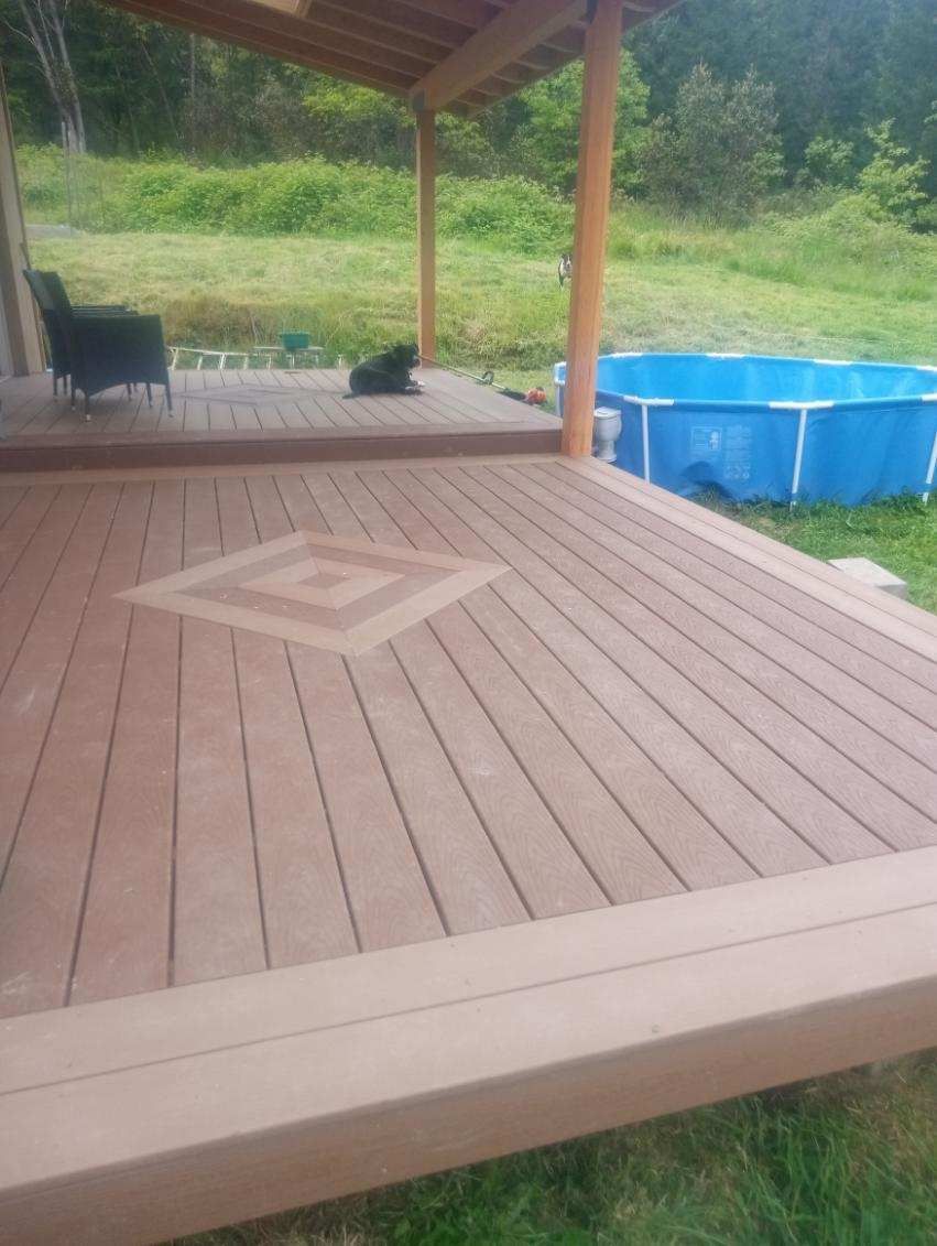 Covered wooden deck with a small black cat, chair, and blue above-ground pool beside a grassy yard