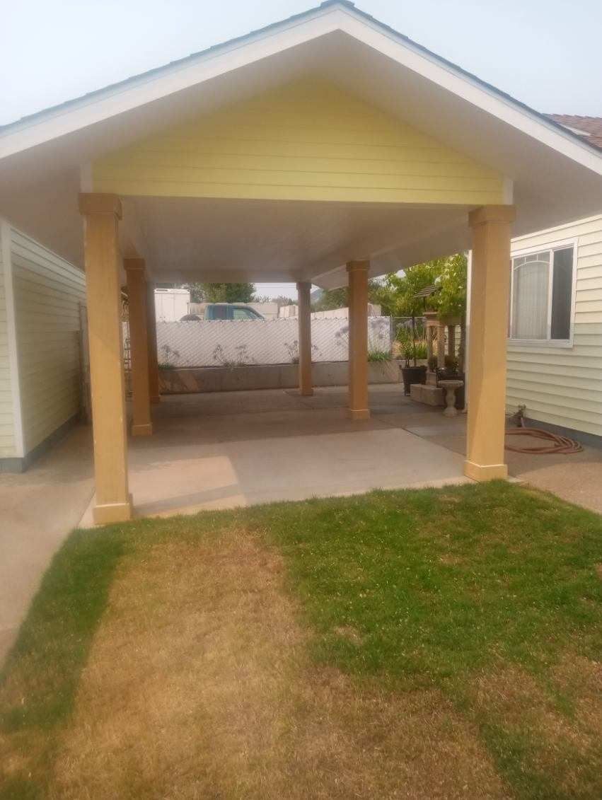 Backyard covered patio with yellow posts and a concrete floor beside a small lawn