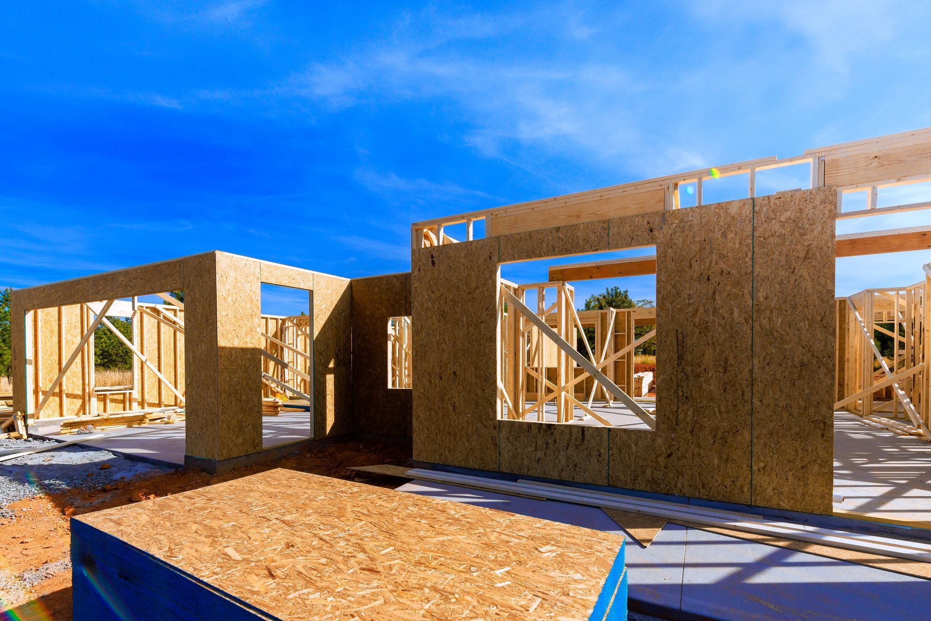 Partially built wooden house framing under a bright blue sky on a construction site